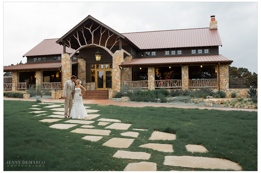 Happy couple stand in front of the beautiful Events Hall at upscale Dripping Springs wedding.
