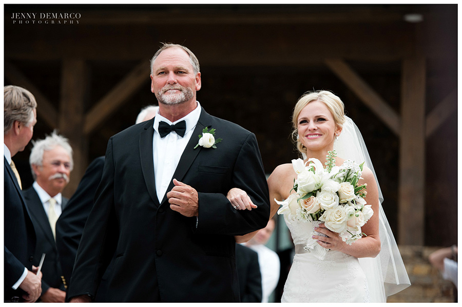 The bride and the father of the bride walk up the aisle in the Members Lodge.