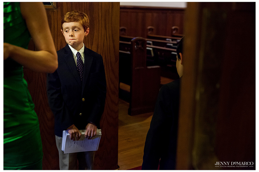 Adorable boy stands with programs in hand by doorway of church.