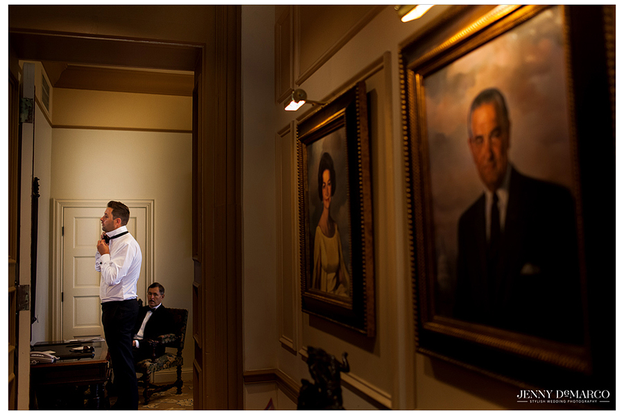 Surrounded by historical portraits at the Driskill, the groom ties his bow-tie in preparation for the big day.