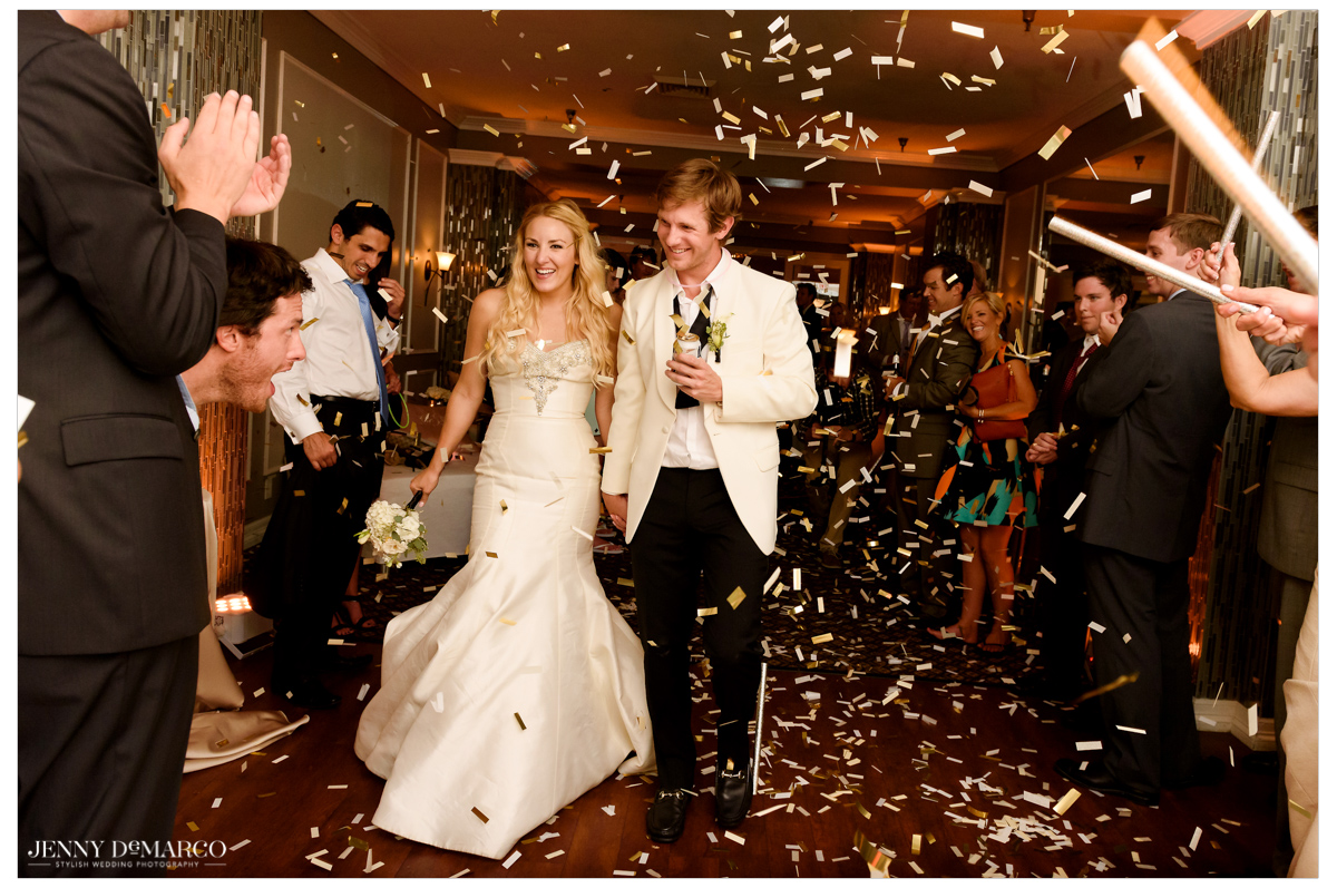 The bride and groom exit the reception as guests pour confetti on the new couple.