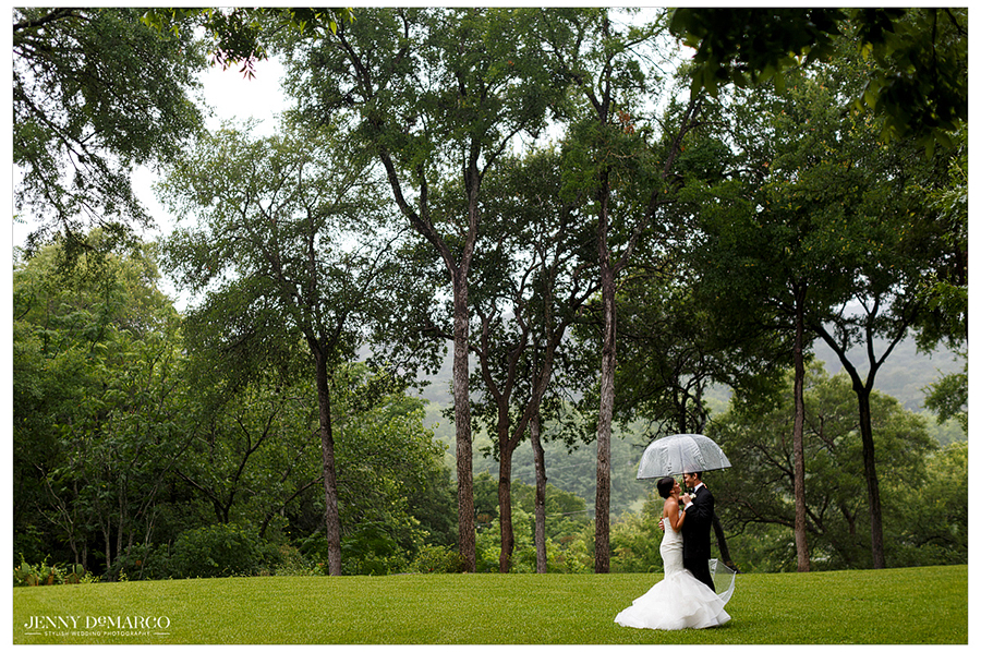 Bride and groom under umbrella in rain after first look 