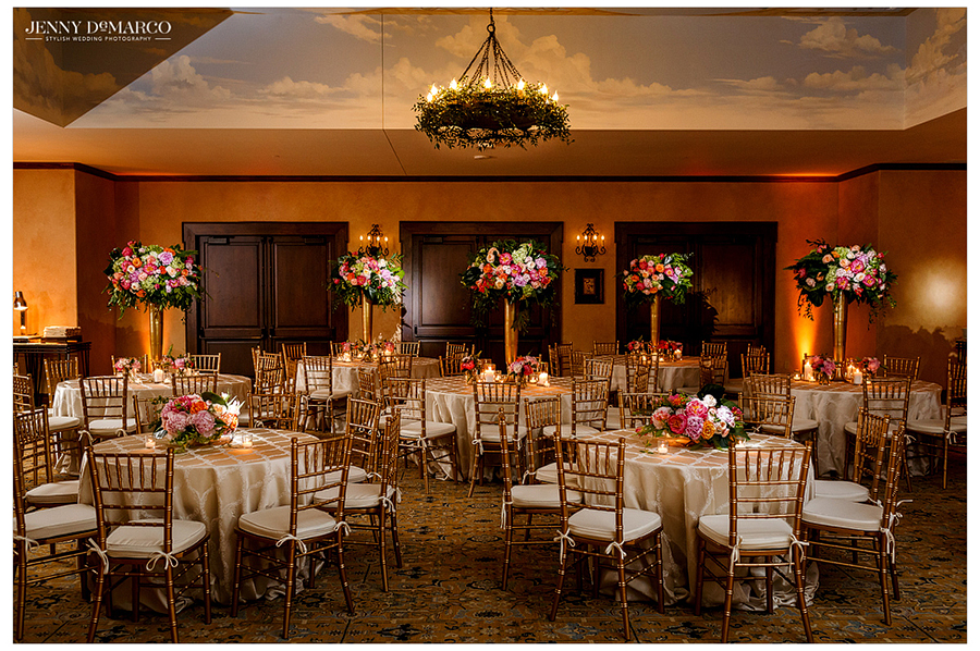 Indoor wedding reception, beautiful gold vases with colorful flowers and white table cloths 