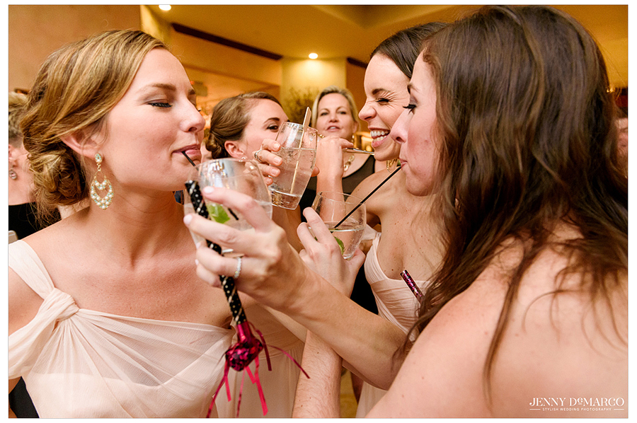 Bridesmaids sip each others drinks on the dance floor 