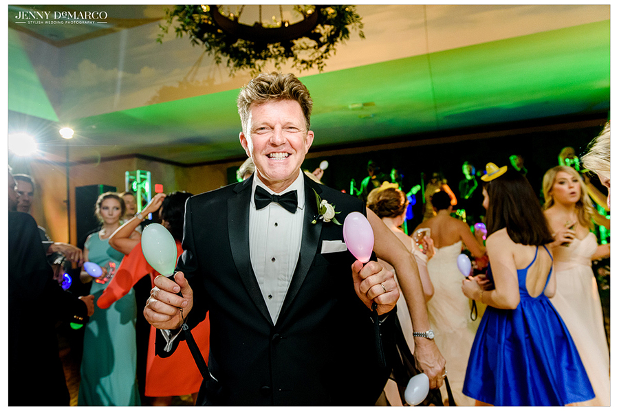 Grooms father holds fun props on dance floor as he dances with other guests 