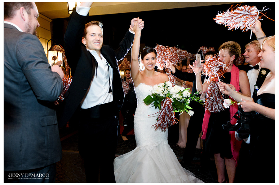 Bride and groom exit reception holding hands high as guests cheer 