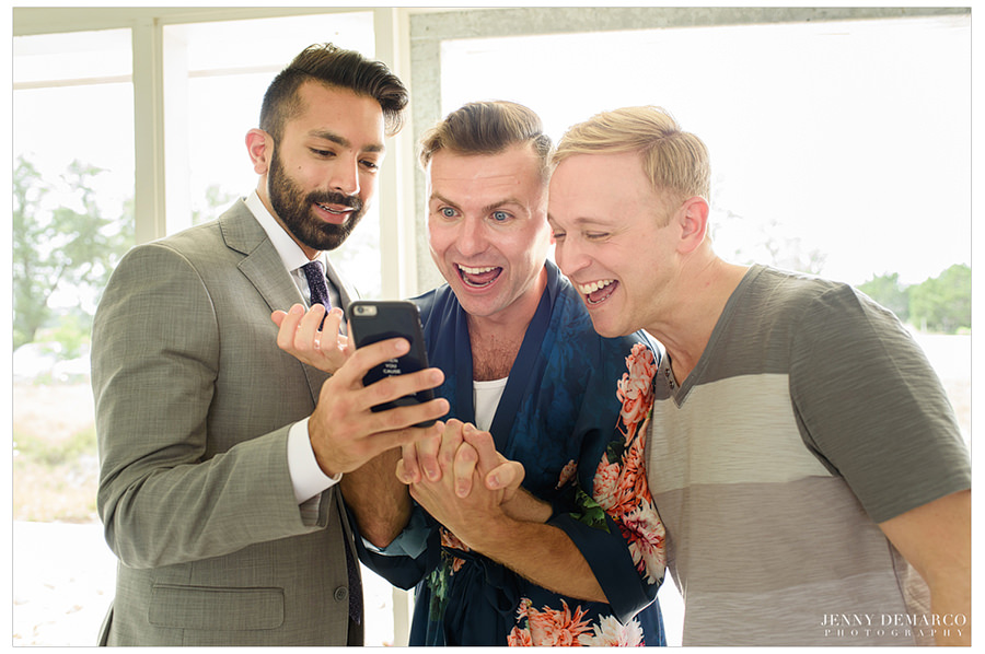 Grooms laughing at a photo with a friend before the wedding.