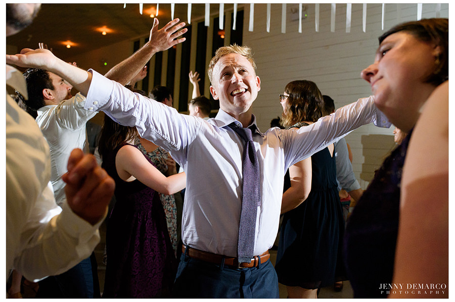 A very happy groom lifts his arms during his wedding reception.