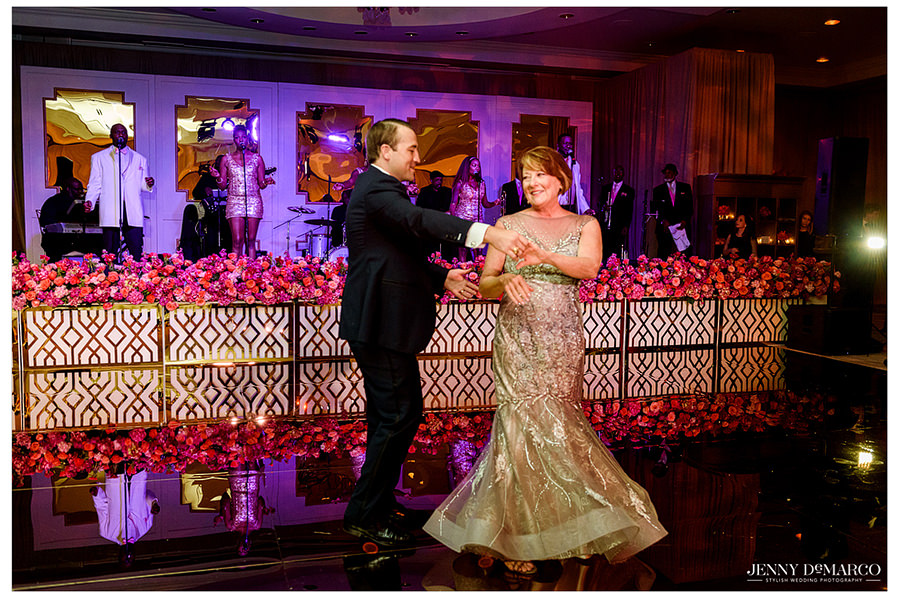 The groom twirls his mother as they dance and she smiles at him.