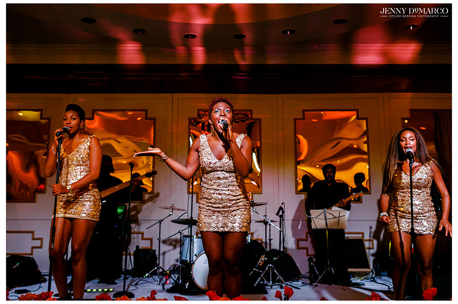 The band performs on stage in sparkly gold dresses and sings to the guests.