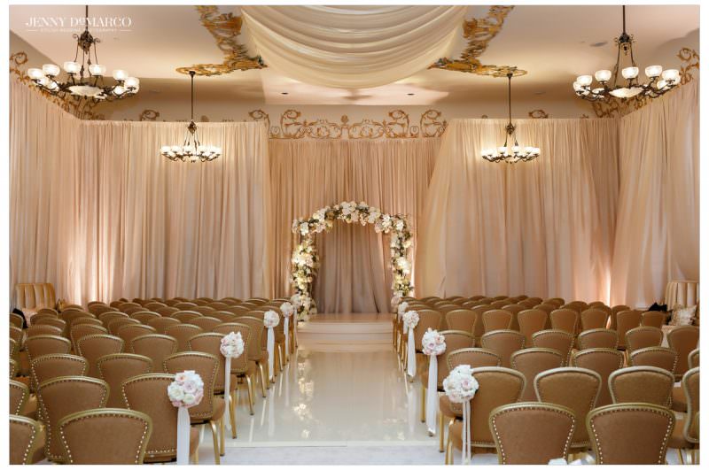 Indoor wedding ceremony setup in the Driskill Ballroom with draping, chandeliers and floral decor
