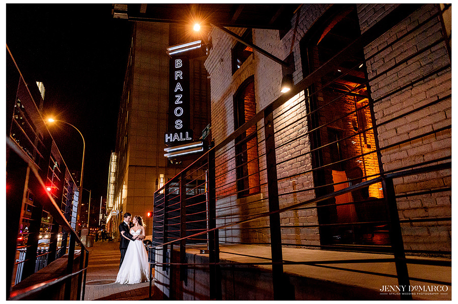 Bride and groom standing under Brazos Hall sign at night.