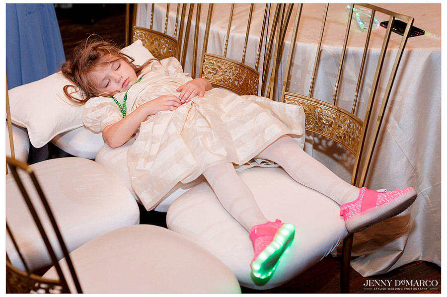 Flower girl was exhausted by the end of the nigh and fell asleep on two chairs with lights on her shoe still blinking after wedding.