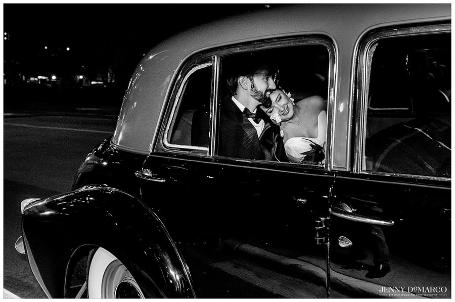 Bride cuddles groom in the back of the get a way car. 