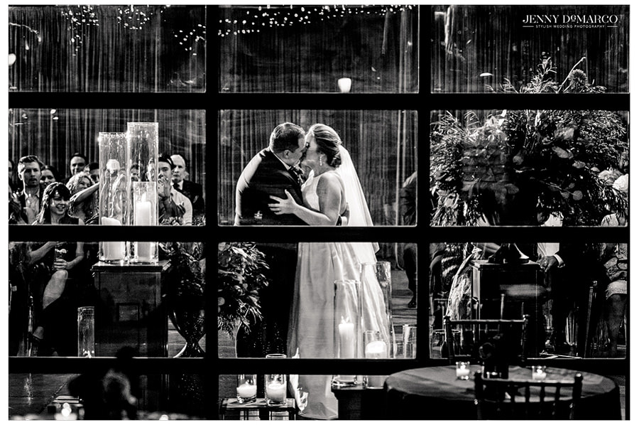 A black and white photo of the bride and groom kissing shot through the window.