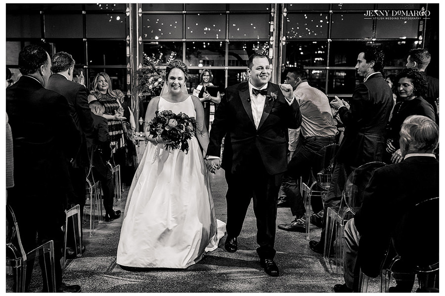 A black and white image of the newlyweds walking down the aisle.