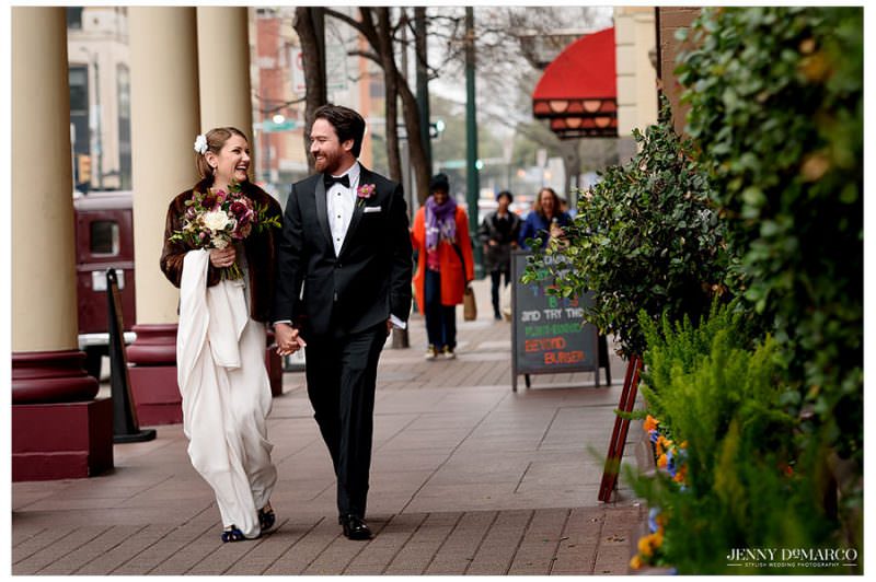 Bride and groom walking along the sidewalk outside The Driskill Hotel in downtown Austin