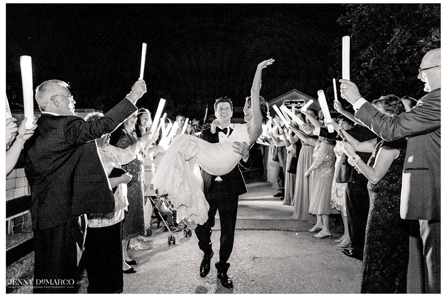 Groom carries his new wife out of the reception while guests cheer.