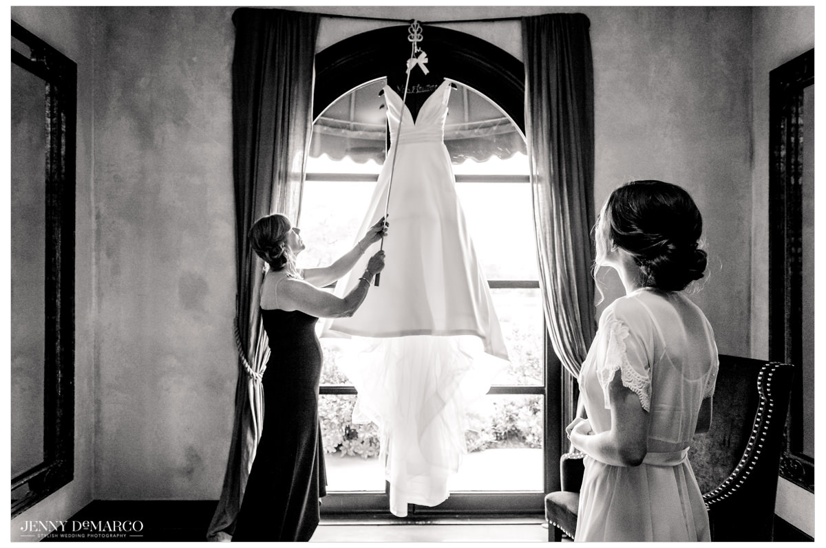 the brides satin white wedding dress hangs above a window.