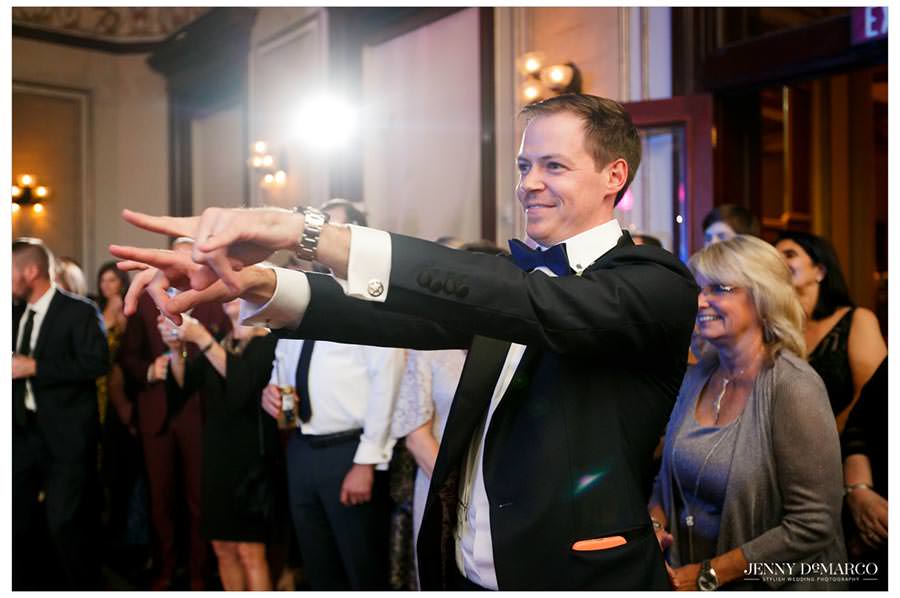 groom pointing to the bride and bridesmaids as they dance for him 