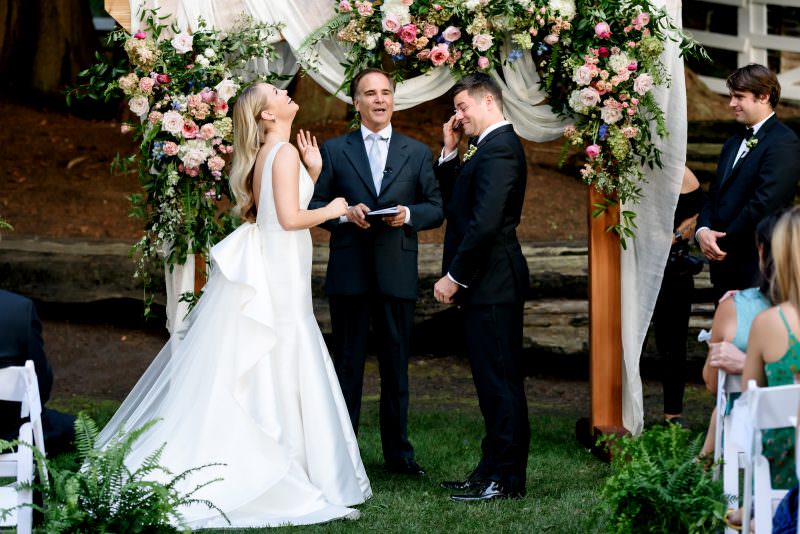 Bride laughing and groom crying at a funny candid moment during the ceremony at Seattle vineyards.
