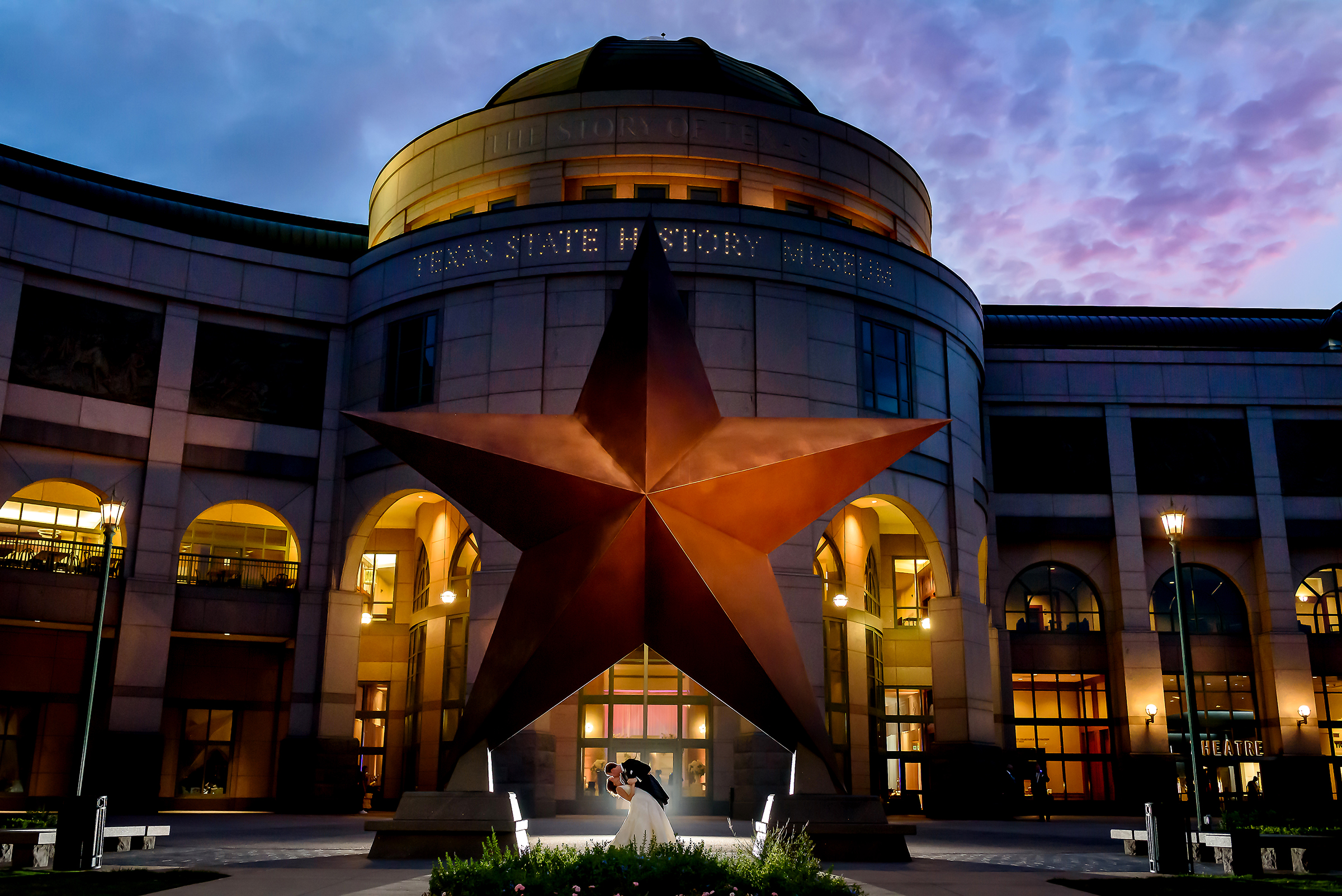 Bride and groom kissing in front of the bob bullock musuem