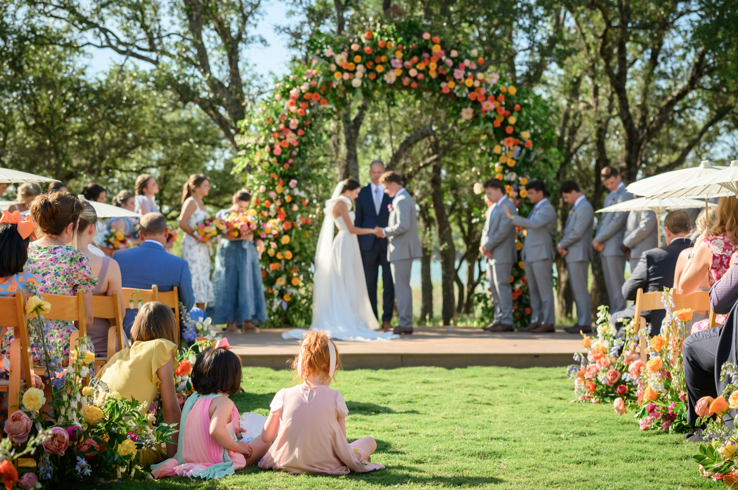 kids sitting in the aisle as the bride and groom hold hands during the ceremony 