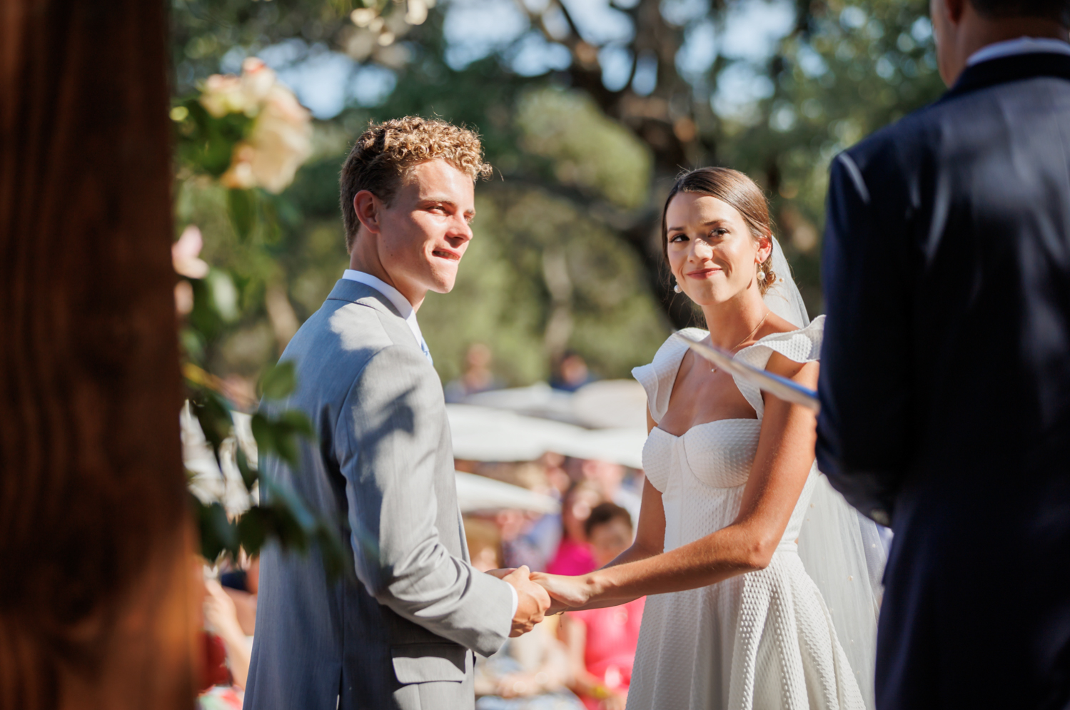 bride and groom holding hands and smiling at the officiant during the wedding 