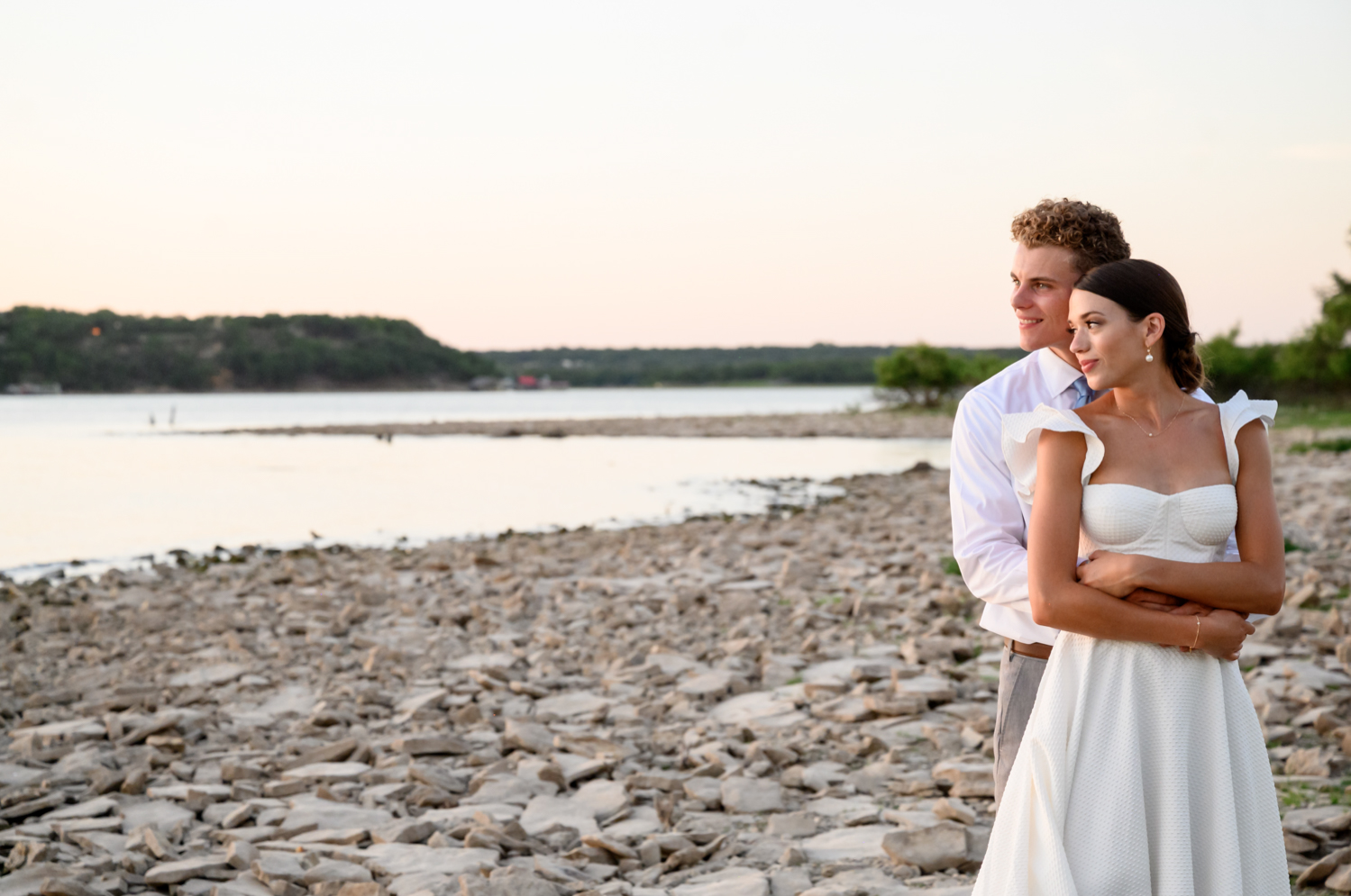 bride and groom hugging looking at the lake during sunset 