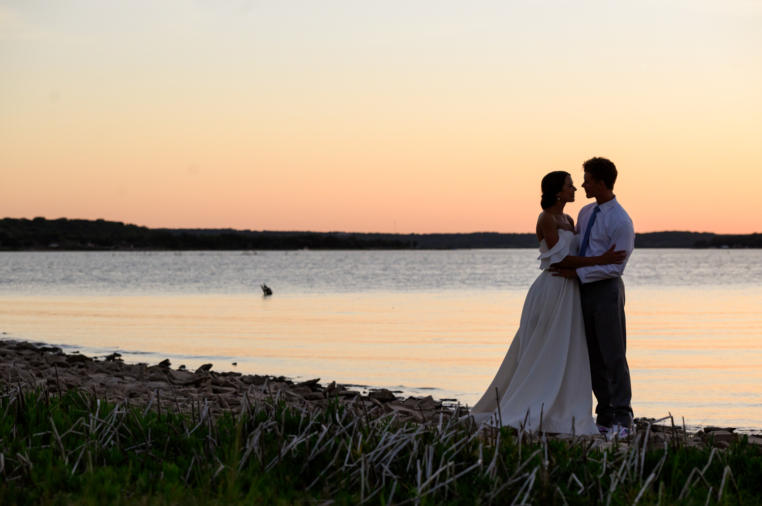 bride and groom looking at each other by the lake during sunset 