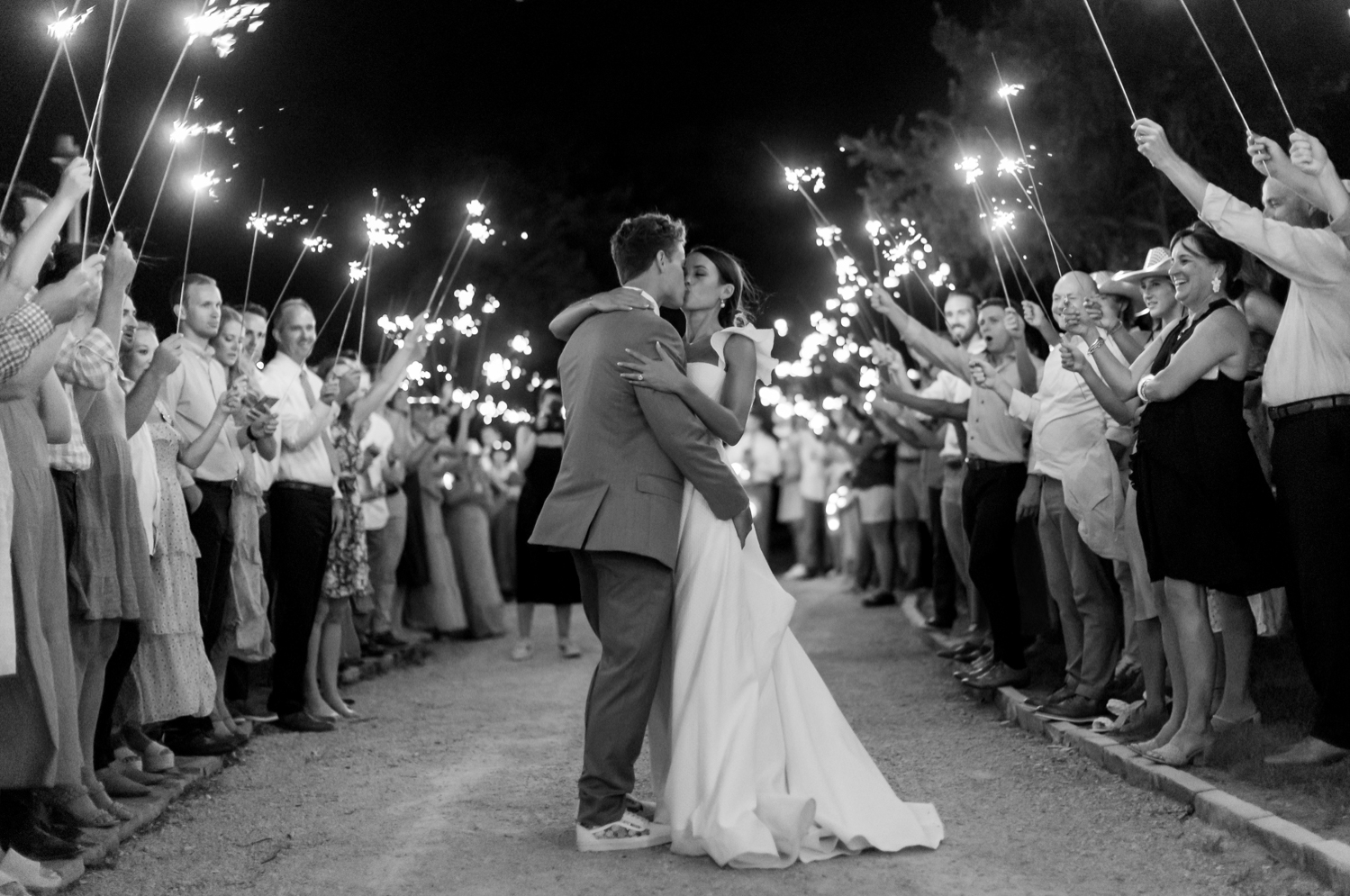 bride and groom kiss while guest line the exit with sparklers 