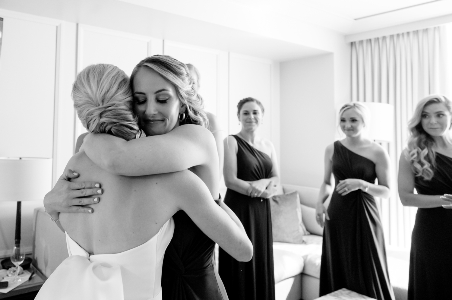 A bridesmaid hugs the bride after she shows them her dress