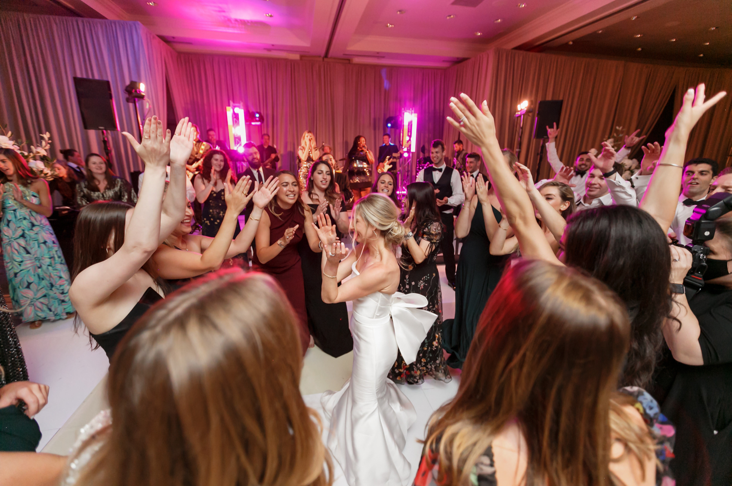 The bride dances as her friends circle around her, clap, and cheer her on