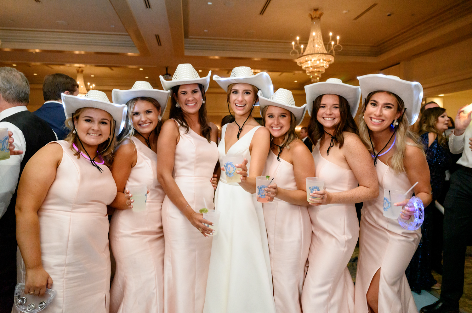 bride with her bridesmaids at the receptions in white light up cowboy hats 