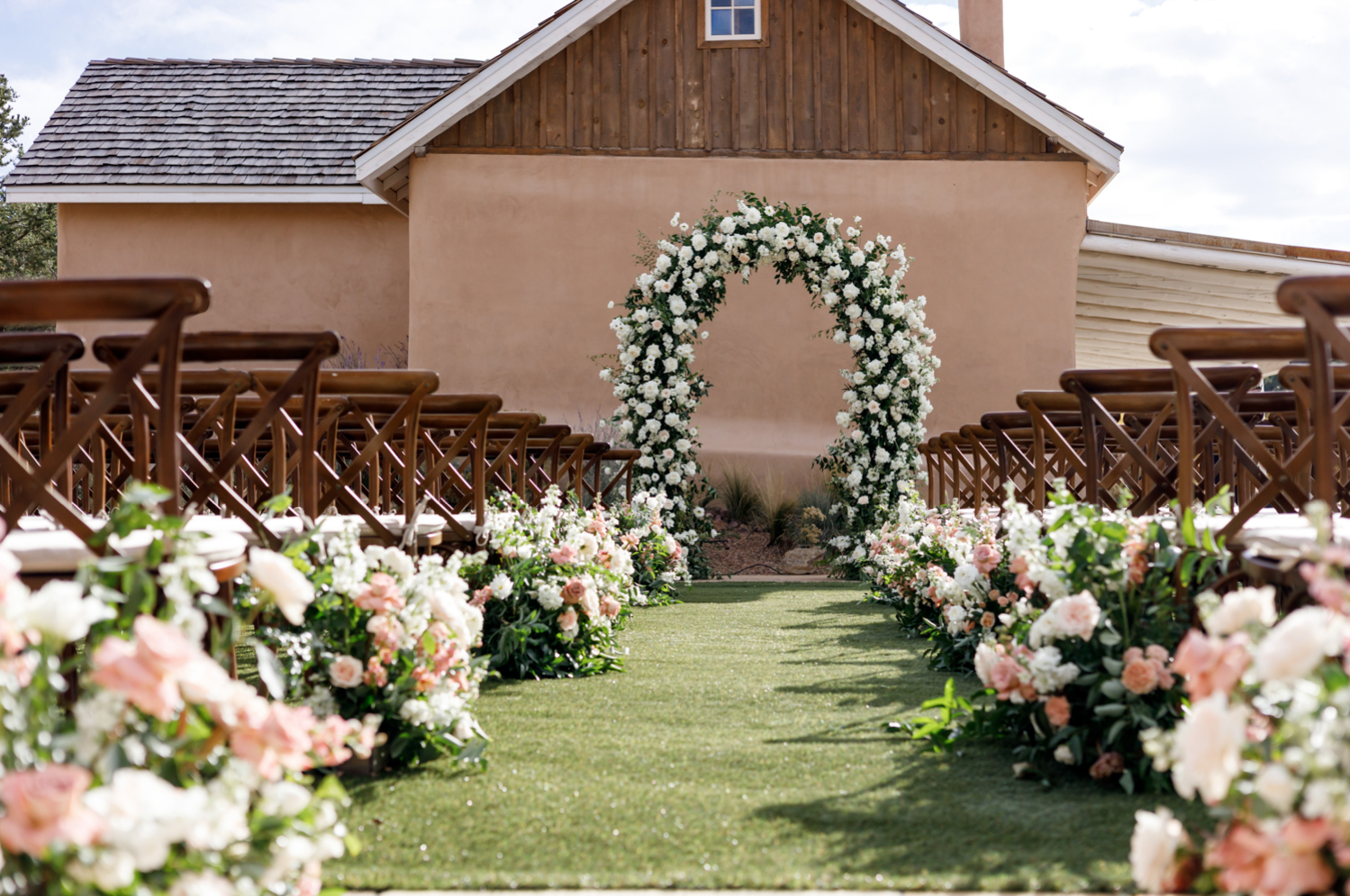 white and pink pastel flowers line the aisle up to the white floral wedding arch 