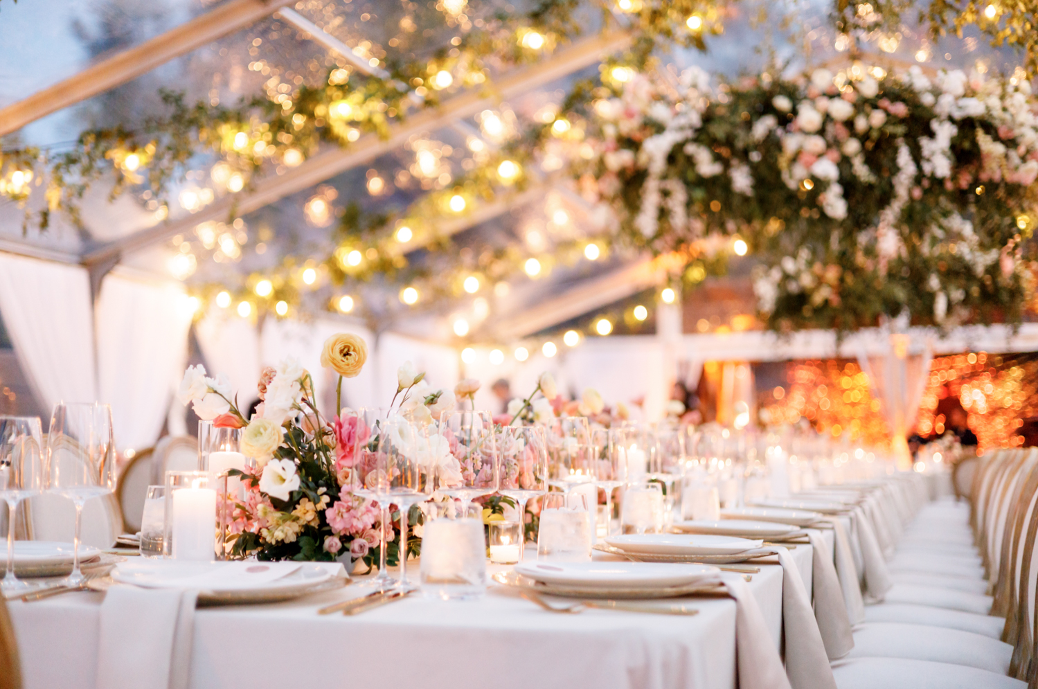 pastel florals line the table at the reception as lights twinkle overhead 