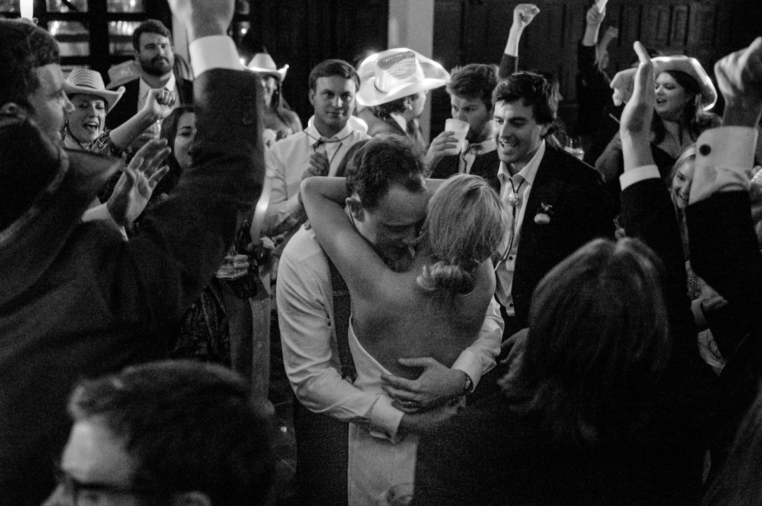 bride and groom hugging while guests dance around them during he reception 