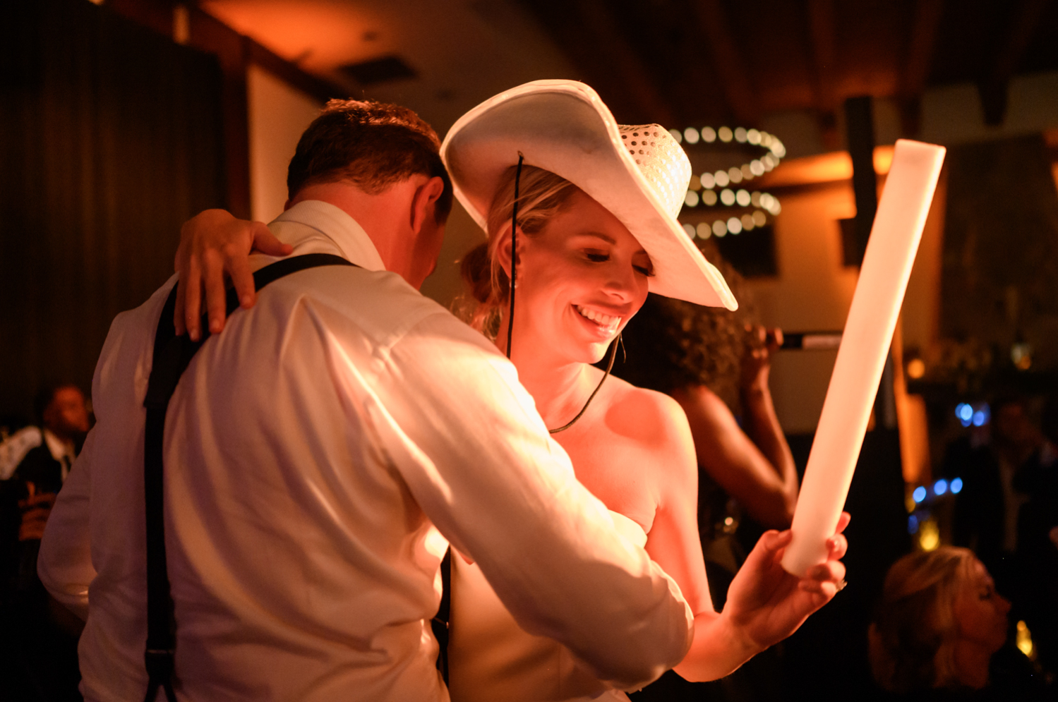 bride and groom dance on stage with the band during the reception with white light up cowboy hats on 