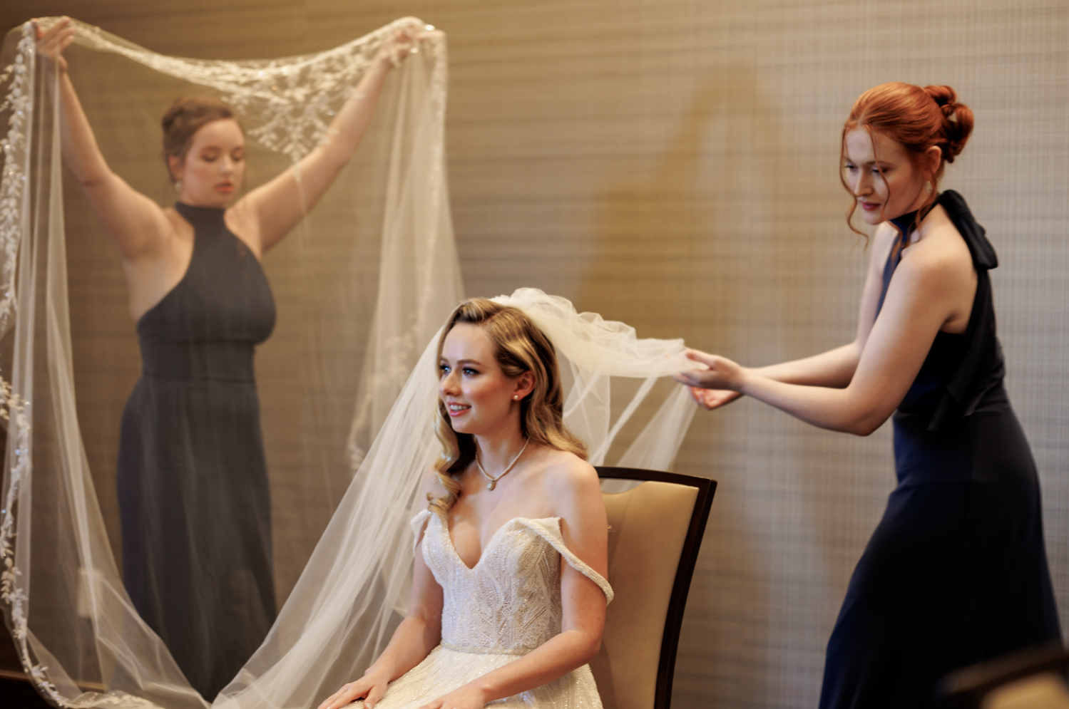 Two bridesmaids fluff the veil and help secure it in the bride's hair