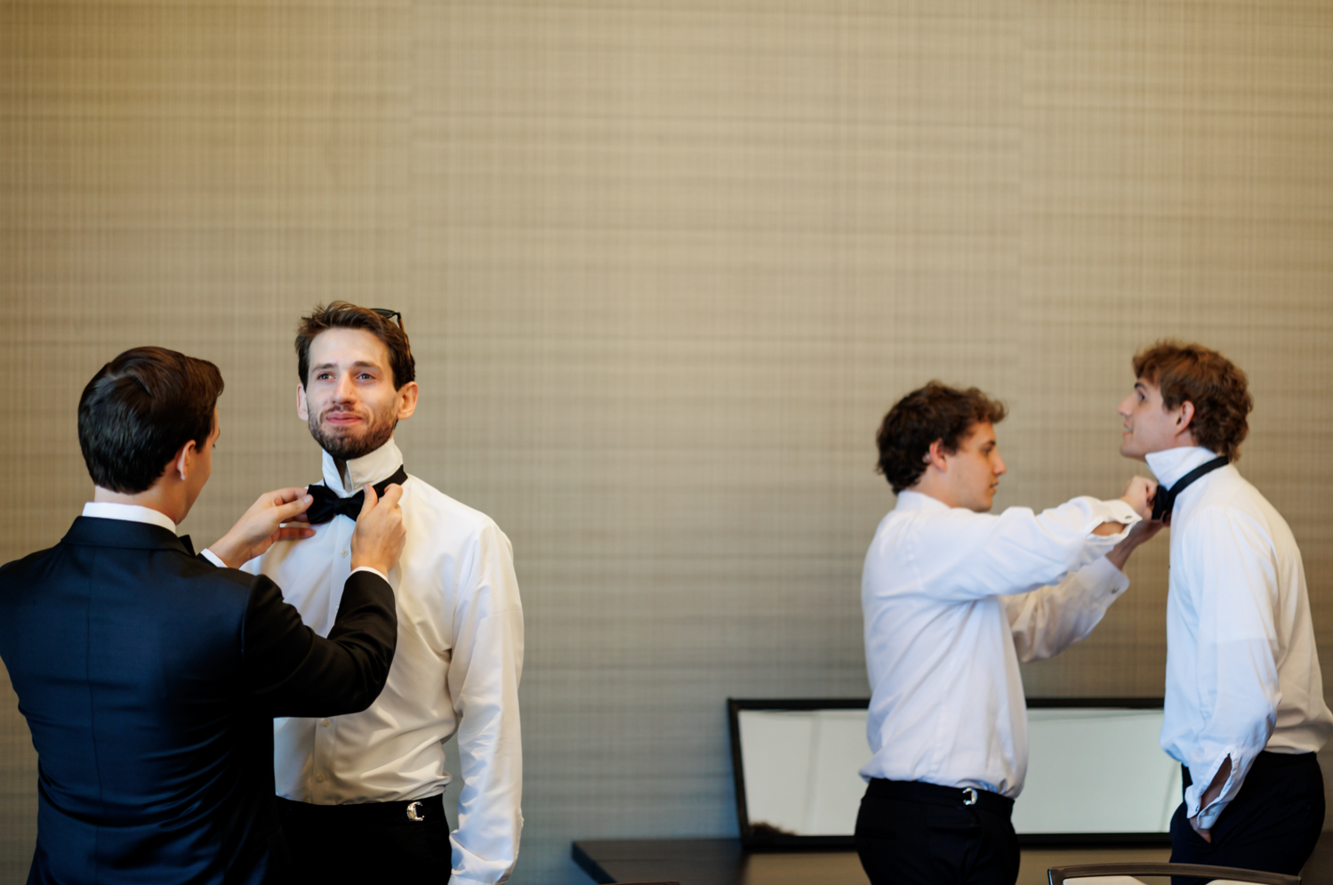 Groomsmen help each other with their bowties in the getting ready suite.