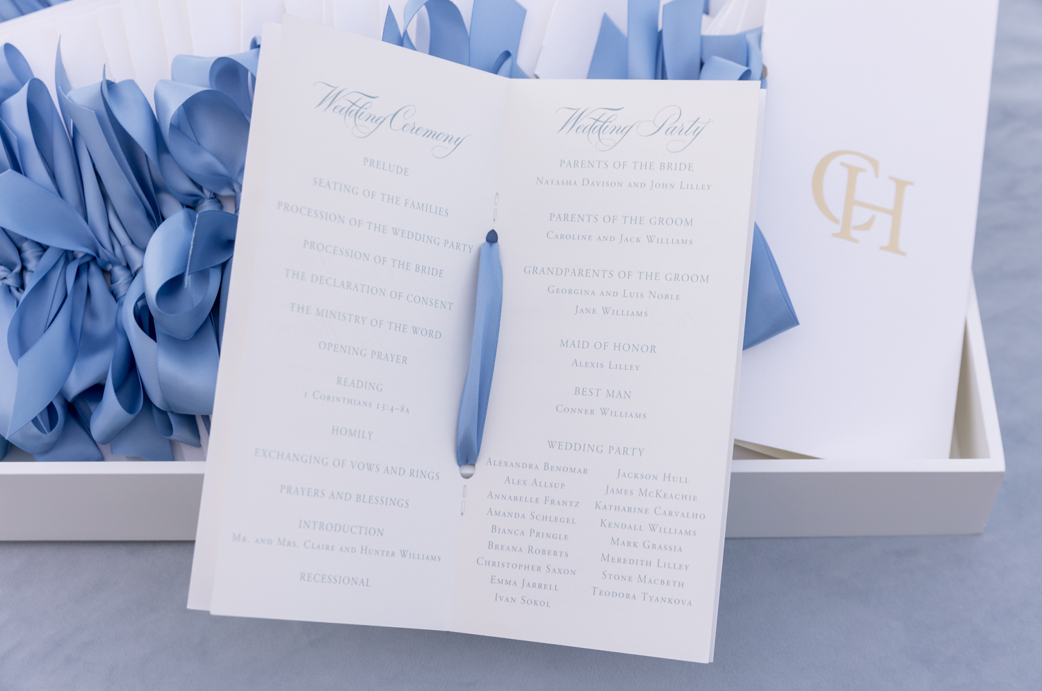 The wedding programs with the ceremony schedule and wedding party. They are white with blue text and a blue ribbon down the seam