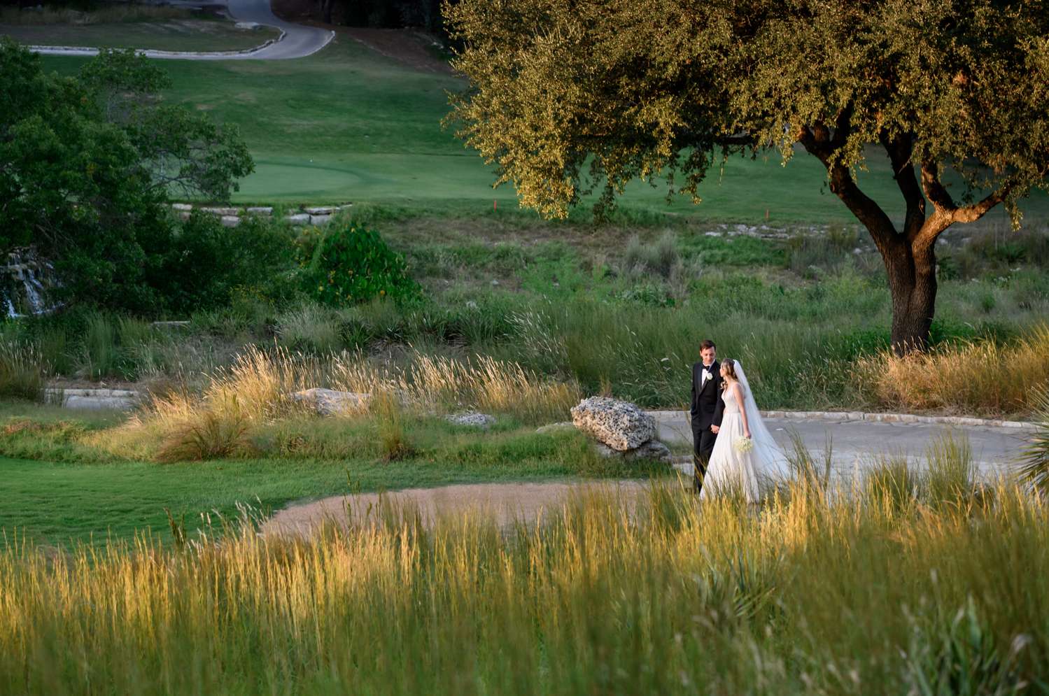 The bride and groom walk through a path on the golf course 