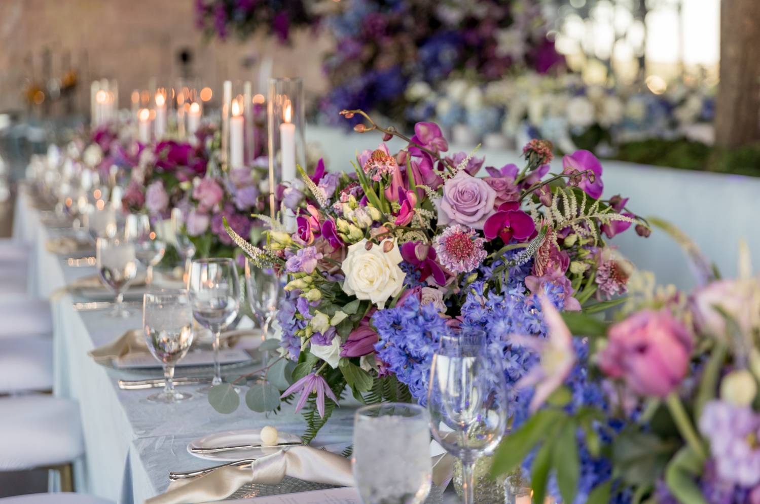 Beautiful blue, purple, and pink flower arrangements and glassware on the dinner tables at the reception.