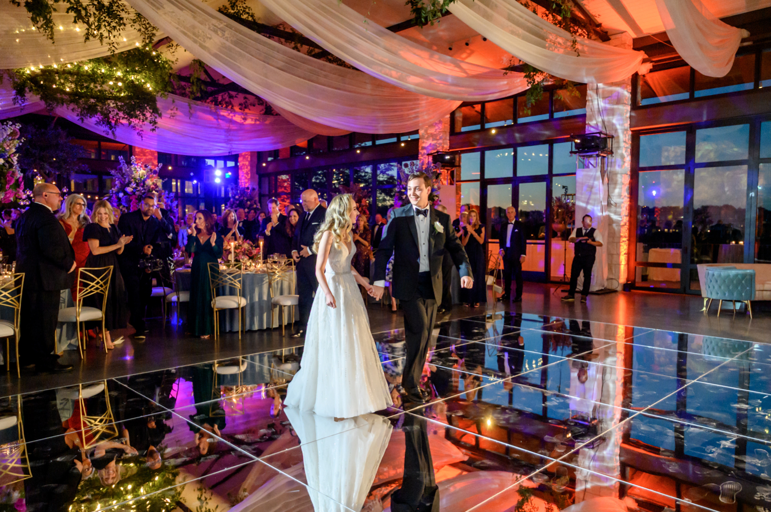 The bride and groom make their way to the shining, reflective dance floor for their first dance.