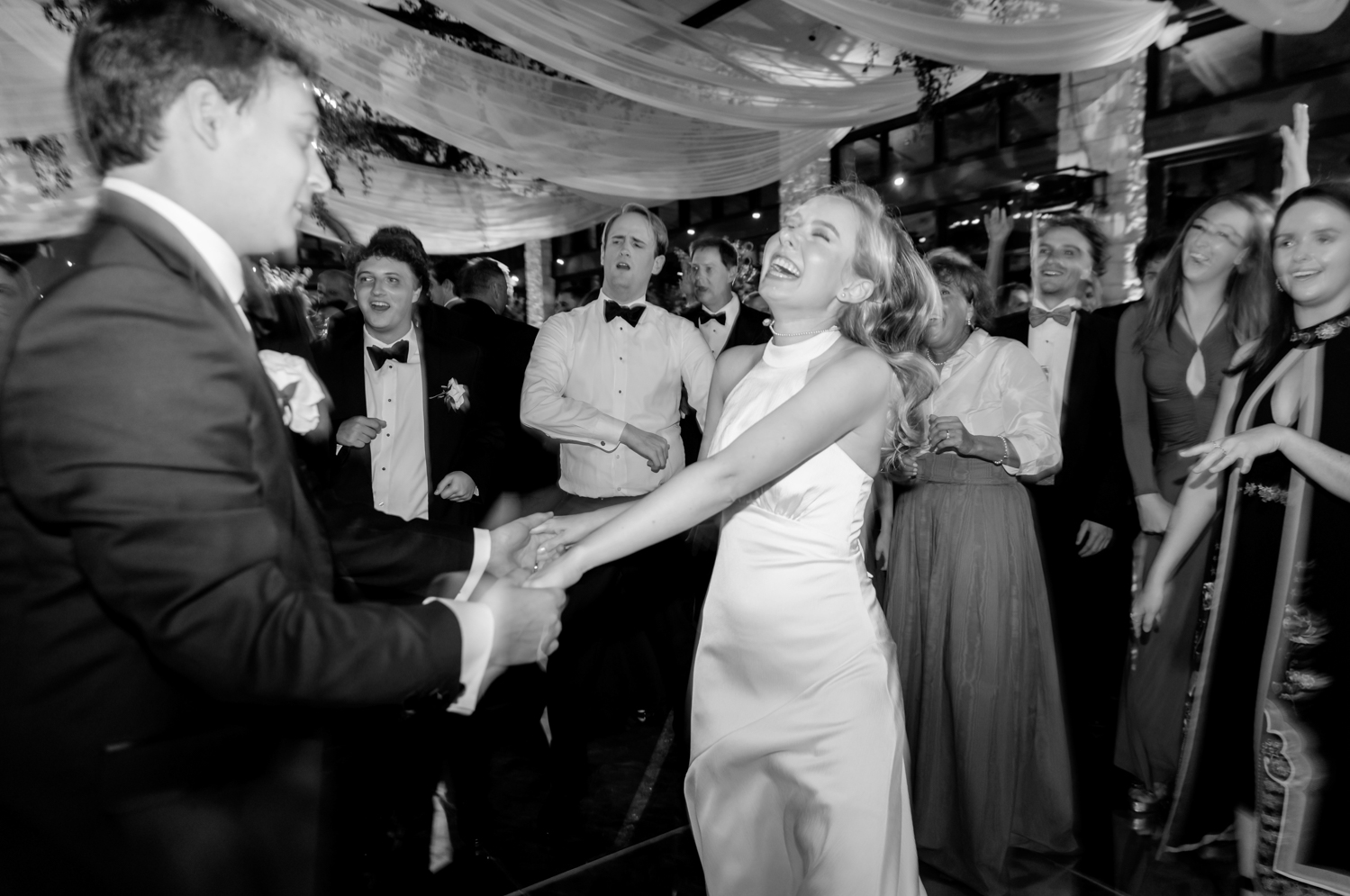 The bride smiles and laughs, dancing with her husband and their guests.
