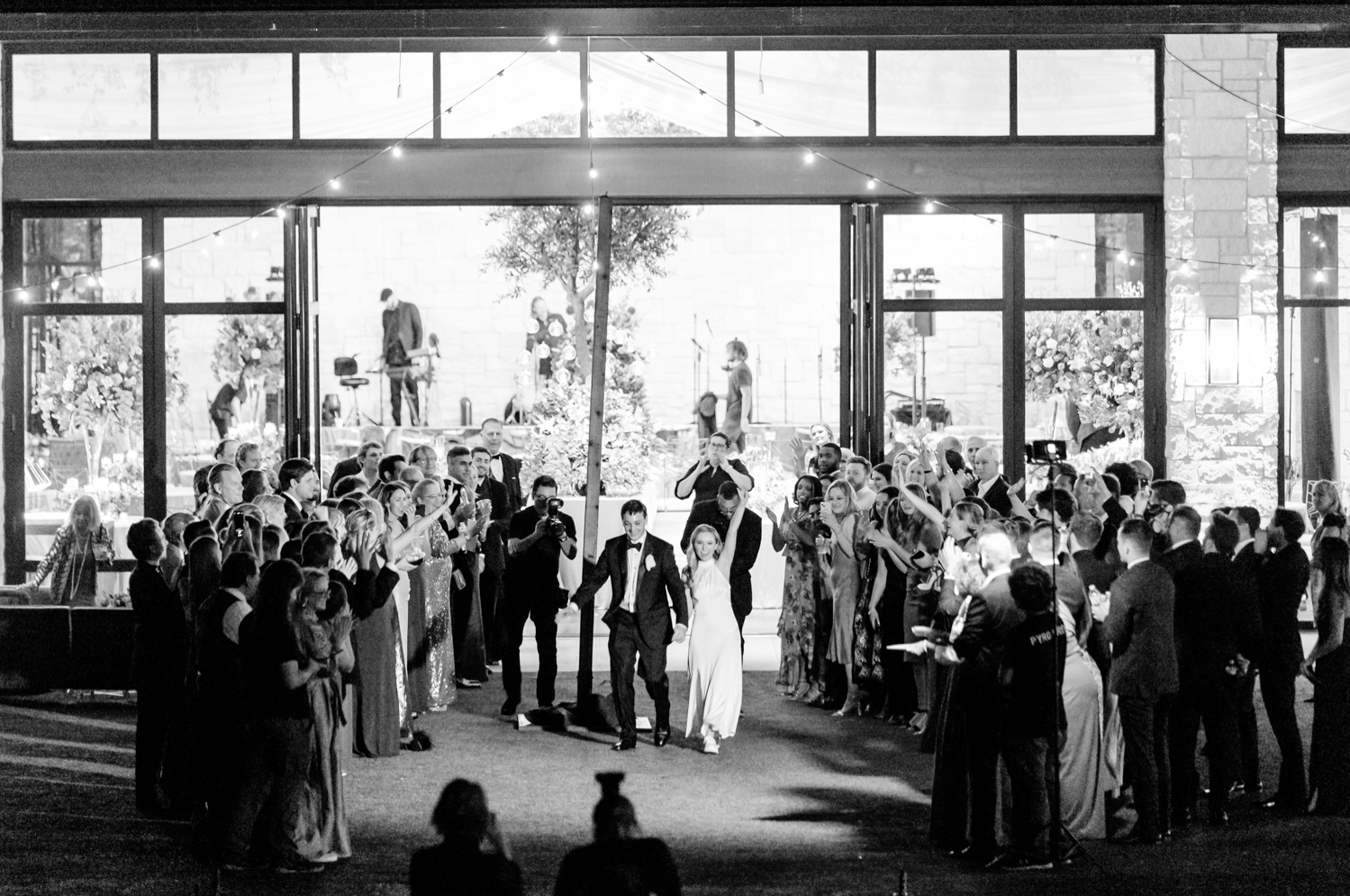 The bride and groom exit the reception as their guests surround them and cheer. 