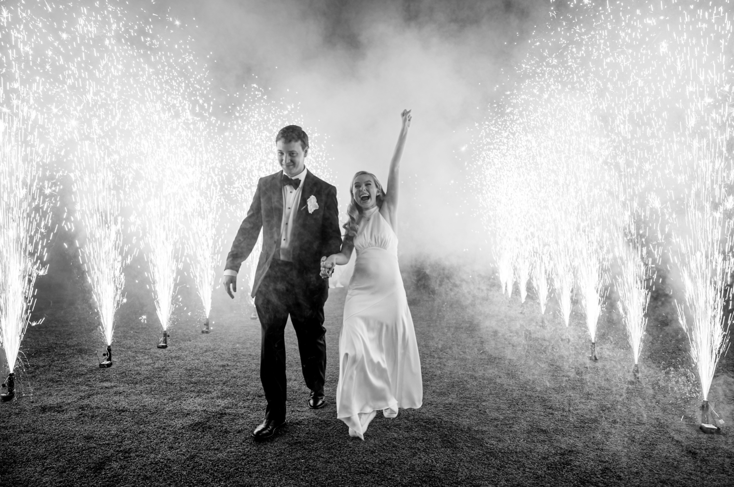 The bride and groom exit the wedding through a tunnel of pyrotechnic sparklers. The bride smiles and pumps her fist in the air in excitement.