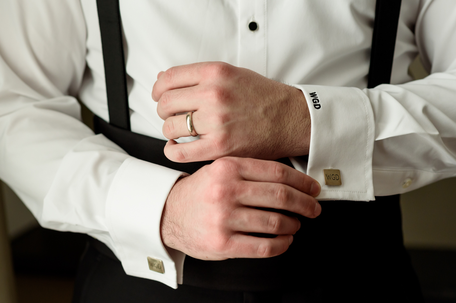 A close up of the grooms hands, showing off his wedding ring, monogrammed dress shirt, and monogrammed cuff links.