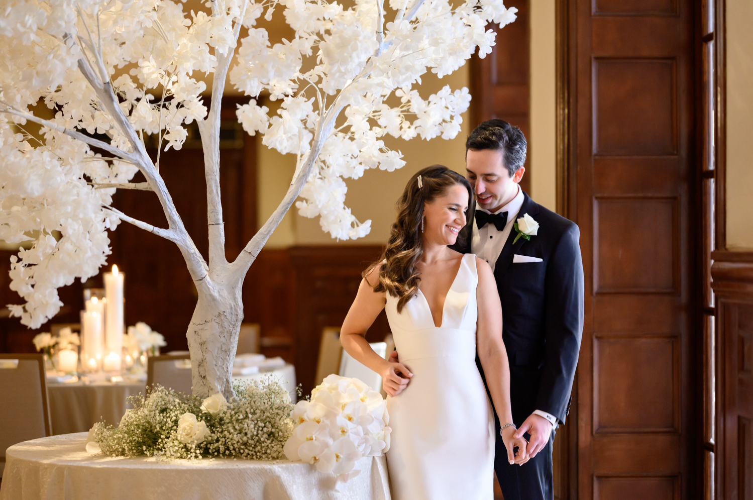 A portrait of the bride and groom in the Driskill hotel in front of a white tree decoration and florals.