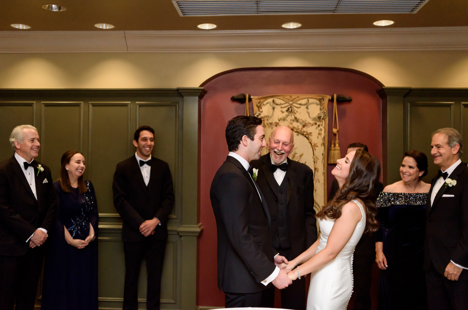 The bride and groom hold hands and laugh with their families during the ketubah ceremony.